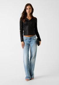 Schwarzes, geripptes Langarmshirt mit Knöpfen, kombiniert mit hellblauen ausgestellten Jeans. Accessoires sind eine schwarze Clutch und offene Schuhe.