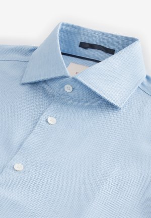 Camisa de vestir para hombre en azul claro con textura, cuello puntiagudo y botones blancos, cuidadosamente doblada sobre un fondo blanco.