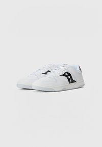 Sneakers bianchi con accenti neri, dotati di una parte superiore in pelle liscia, punta arrotondata e suola in gomma texturizzata. I lacci sono piatti e intrecciati.