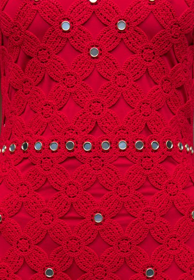 Κόκκινο ύφασμα με περίπλοκο κεντητό λουλουδάτο πλέγμα και μικρές στρογγυλές μεταλλικές καρφίτσες τοποθετημένες σε σειρές σε όλο το σχέδιο.