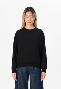 Zwarte sweatshirt met een ronde hals en lange raglanmouwen. Voorzien van een subtiele, gegraveerde logo aan de voorkant, gecombineerd met een ontspannen pasvorm denim.