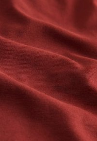 Tessuto rosso a costine con fini striature verticali, che mostra una texture liscia e un aspetto morbido, catturando la luce in onde sottili.