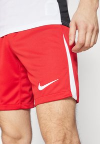 Rode Nike sportshorts met witte accenten, voorzien van een textuurstof en een zijsplit voor bewegingsvrijheid. Logo weergegeven op de zoom.