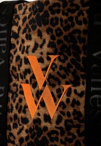 Tela con estampado de leopardo con base marrón texturizada y manchas negras. Presenta un logotipo "W" bordado en naranja sobre el patrón.