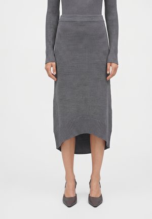 Mujer con falda midi de punto acanalado gris con dobladillo curvo, combinada con un top de manga larga a juego y zapatos de tacón gris de punta afilada.