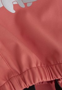 Korallfärgad tyg med en slät yta, med en samlad elastisk nederkant och svarta dragsnören, accentuerad av en vit grafisk design.