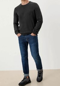 Czarny sweter z ribbowym wykończeniem rękawów i dekoltu, zestawiony z obcisłymi niebieskimi dżinsami z podwiniętymi nogawkami oraz szarymi butami sportowymi.