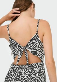 Vestido de rayas de cebra en blanco y negro con lazo en la espalda, tirantes finos y lados con corte. Tejido suave con una textura lisa.