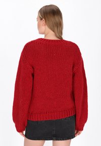 Flauschiger roter Strickpullover mit einem gerippten Ausschnitt und übergroßen Ärmeln, ausgestattet mit einem strukturierten Stoff und einem geraden Saum auf Taillenhöhe.