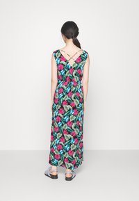 Maxiklänning med svart bakgrund och färgglada tropiska blad- och blommönster. Korsa axelband och en figurnära midja. Bärs med platta sandaler.