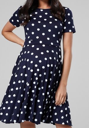 Marineblaues Baumwollkleid mit weißen Polka-Dots, ausgestattet mit kurzen Ärmeln, einem taillierten Oberteil und einem ausgestellten Rock. Glatte Textur mit klassischem Design.