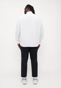 Camicia bianca a maniche lunghe con orlo dritto e dettagli ai polsini con bottoni, abbinata a pantaloni neri sartoriali e sneakers chiare.