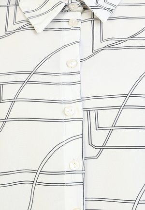 Blouse blanche avec un motif linéaire noir, dotée d'un col pointu, d'une fermeture à bouton avec des boutons ronds et d'un tissu lisse et léger.