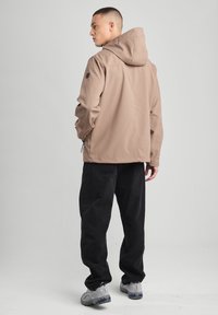 Tan hooded jacket with a smooth texture, adjustable hem, and black accents, paired with loose black pants and sneakers.