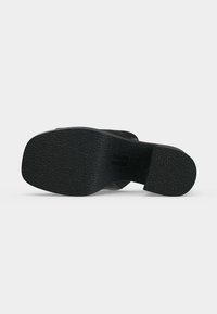 Semelle de chaussure noire avec grip texturé montrée par le dessous sur un fond clair uni.