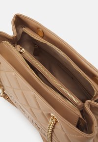 Quilted beige handbag with gold hardware, featuring multiple interior compartments and zippers, and a magnetic snap closure.