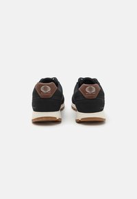 Black athletic shoes with a textured leather and fabric material, featuring brown accents on the heel, and a white midsole and sole.