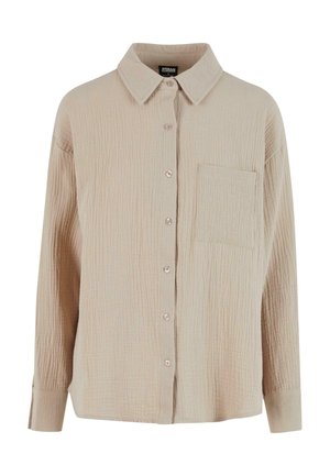 Beige button-up shirt made of textured fabric with a crinkled appearance. Features a collar, long sleeves, and a single chest pocket.