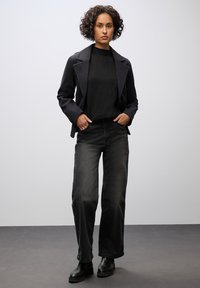Blazer nero su misura sopra un maglione nero, abbinato a jeans neri a vita alta e gamba larga e stivaletti. Tessuto liscio con design strutturato.
