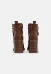 Bottines en cuir marron avec un design structuré, présentant une sangle avec des détails en métal et un talon en bloc texturé.
