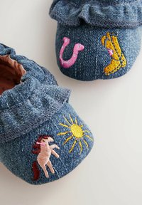 Botines de mezclilla para bebé con un cuello con volantes, que presentan coloridos diseños bordados: un caballo, un sol, una herradura rosa y botas amarillas.