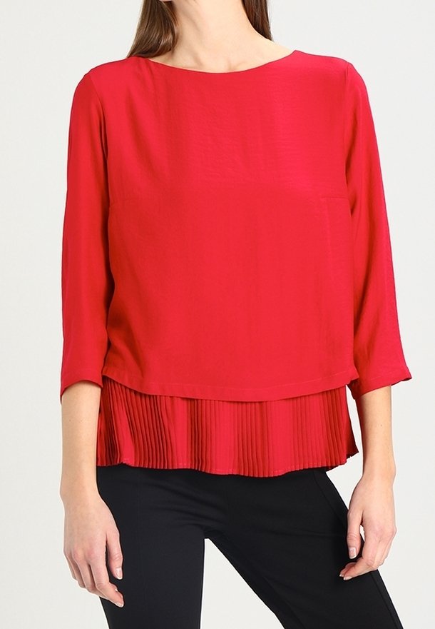 Blouse rouge avec un col rond et des manches trois-quarts. Présente une couche plissée au niveau de l'ourlet. Texture de tissu lisse, design décontracté.