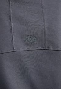 Sivi atletski materijal s glatkom teksturom i vidljivim šavovima. Sadrži mali otisnuti logotip "The North Face" u kutu.