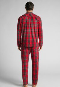 Červený kostkovaný pyžamový set obsahující košili na knoflíky s dlouhými rukávy a odpovídající kalhoty. Materiál vypadá měkký s kartáčovanou texturou.