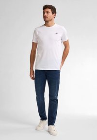 Bílé tričko s krátkým rukávem s malým logem na hrudi, doplněné tmavě modrými džínami a bílými teniskami. Neformální střih, jednobarevný design.