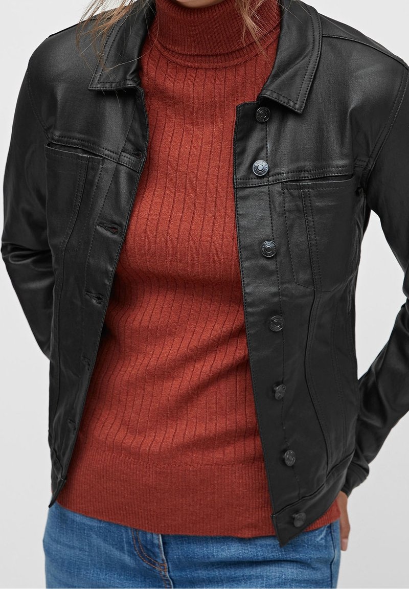 Chaqueta de cuero negra con un cierre de botones en la parte delantera, bolsillo en el pecho y un diseño estructurado, superpuesta sobre un cuello de tortuga de color óxido con ribetes.