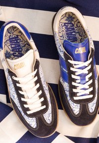 Paire de baskets à motifs avec des détails bleus, blancs et noirs, lacets blancs et logo doré « CAVAL » sur la languette et les semelles intérieures en tissu rayé.