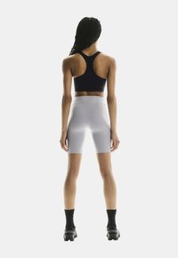 Zwarte sportbeha en lichtgrijze hoge fietsbroek. De broek heeft een gladde textuur, terwijl de beha een sportieve rugontwerp heeft.