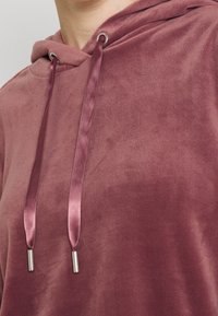 Felpa con cappuccio color bordeaux realizzata in morbido e lussuoso tessuto. Presenta lacci in satin con punte in metallo e una vestibilità comoda.