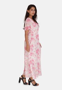 Robe maxi florale en rose clair avec des motifs roses et dorés. Présente des manches courtes, une taille élastique et un tissu fluide. Associée à des talons blocs noirs.