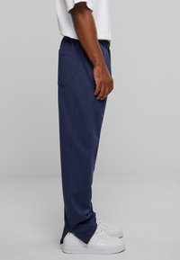 Marineblaue Sweatpants mit einer lockeren Passform, elastischem Taillenbund, Seitentasche und belüfteten Säumen, kombiniert mit weißen Sneakers.