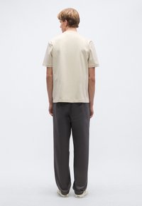 Μπεζ κοντομάνικο T-shirt με ίσια γραμμή, συνδυασμένο με σκούρο γκρι παντελόνια σε χαλαρή εφαρμογή. Καθημερινό σχέδιο με μαλακή υφή.