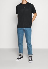 Svart nätkortärmad skjorta med en vit Nike-logotyp, tillsammans med ljusblå raka jeans och svarta sneakers med vita snörningar.
