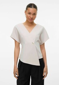 Lys beige omslagsbluse med V-hals, korte ermer og asymmetrisk skjæring, med et gullfarget knappeakcent foran.