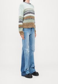 Strickpullover in pastellfarbenen Streifen aus Grün, Weiß, Braun und Grau. Kombiniert mit hellblauen, ausgestellten Jeans und klobigen, schwarzen Plateauschuhen.