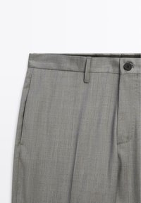 Grau zugeschnittene Hose mit glatter Textur, flachem Frontdesign, Seitentaschen und Knopfverschluss. Verfügt über ein dezentes gewebtes Muster.