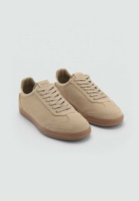 Sneaker in suede beige con un design a profil basso, punta rotonda, lacci piatti e una suola in gomma marrone texturizzata. Finitura liscia con cuciture sottili.