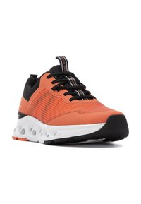 Zapatilla deportiva con parte superior de malla negra y naranja brillante, media suela blanca, superficie texturizada, patrones intrincados y una lengüeta en el talón.