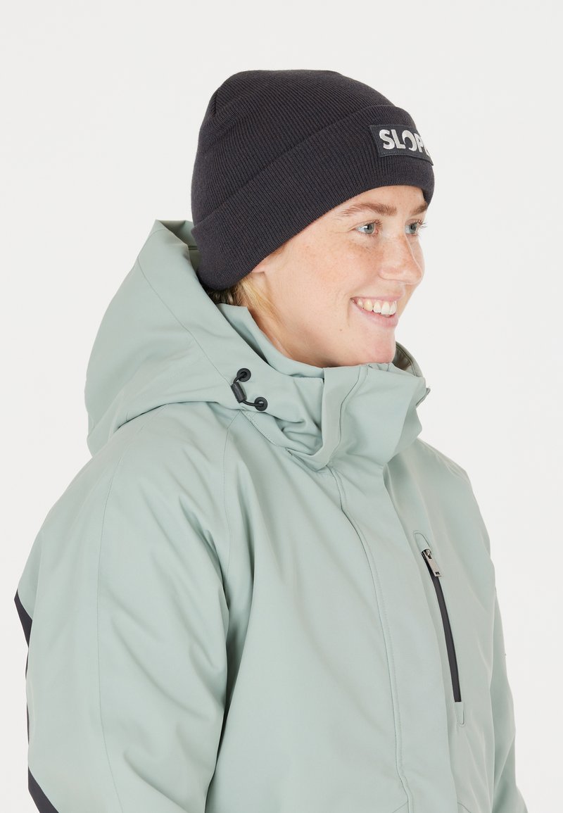 Ljusgrön huvajacka med svarta detaljer; dragkedjeficka och justerbar huva. Matchad med en mörk mössa med en logotypapplikation.