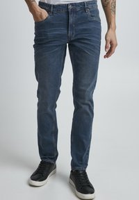 Jeans iz denima v temno modri barvi, zožene zasnove z rahlim izginjanjem, pet žepov in kontrastnim šivanjem. V kombinaciji s črnimi supergami.