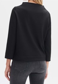 Felpa nera a trama con maniche a tre quarti, scollatura rotonda e vestibilità rilassata. Vista da dietro abbinata a jeans grigi.
