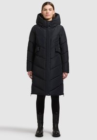 Mustast pufferjopes on kõrge kaelusega kapuuts, vertikaalne ja horisontaalne ševronite õmblus, kaks küljetaskut ja tõmblukuga ventilatsiooni sulgemised äärel.