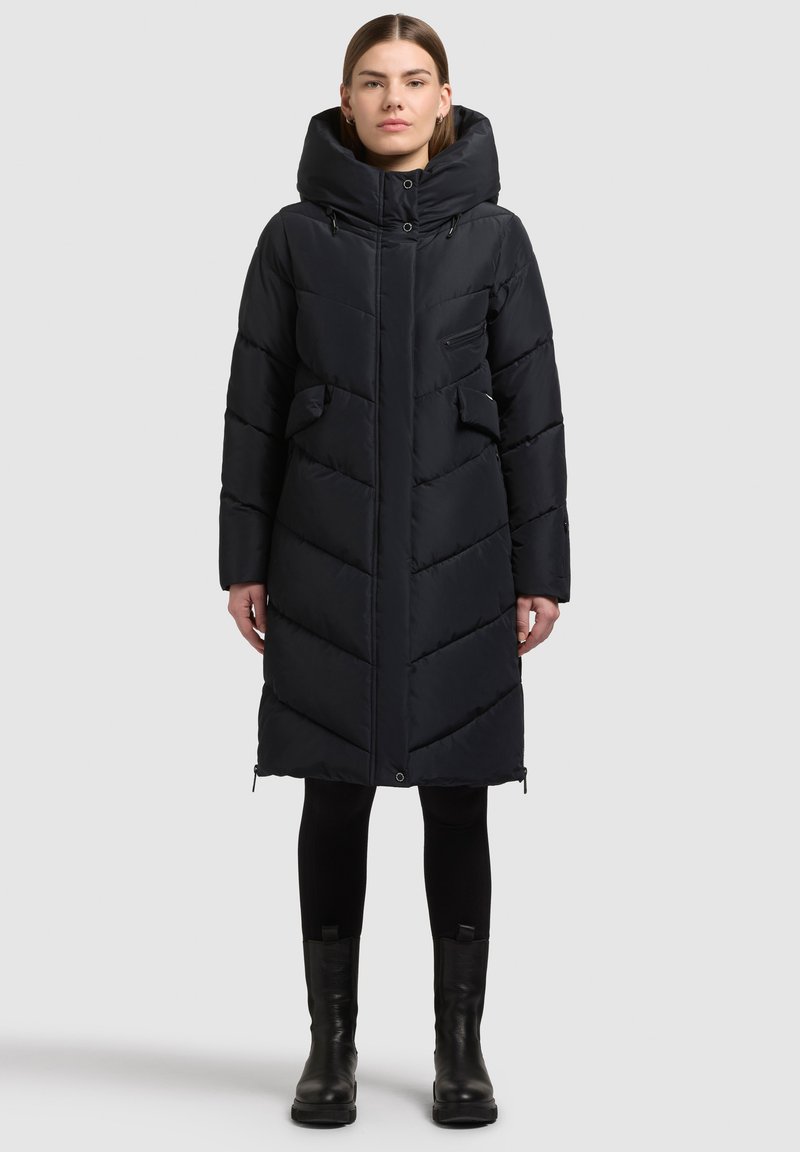 Mustast pufferjopes on kõrge kaelusega kapuuts, vertikaalne ja horisontaalne ševronite õmblus, kaks küljetaskut ja tõmblukuga ventilatsiooni sulgemised äärel.