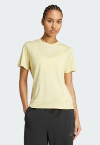 Hellgelbes sportliches T-Shirt mit kurzen Ärmeln, rundem Halsausschnitt und dezentem Logo auf der Brust. Glatte Textur, taillierte Passform, minimalistischer Stil.