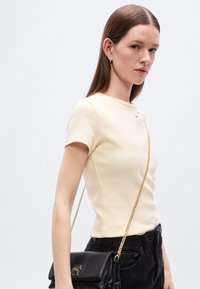 Φόρεμα σε εκρού χρώμα με κοντά μανίκια, με ριμπ υφή και διακριτική λεπτομέρεια λογότυπου. Συνδυασμένο με μαύρα ψηλόμεσα τζιν παντελόνια και μαύρη τσάντα χειρός.