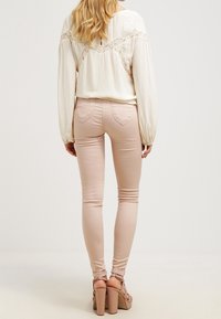 Krämlangärmad blus med spetsdetaljer, matchad med ljusrosa skinny jeans och beige blockklacksandaler, sett bakifrån.